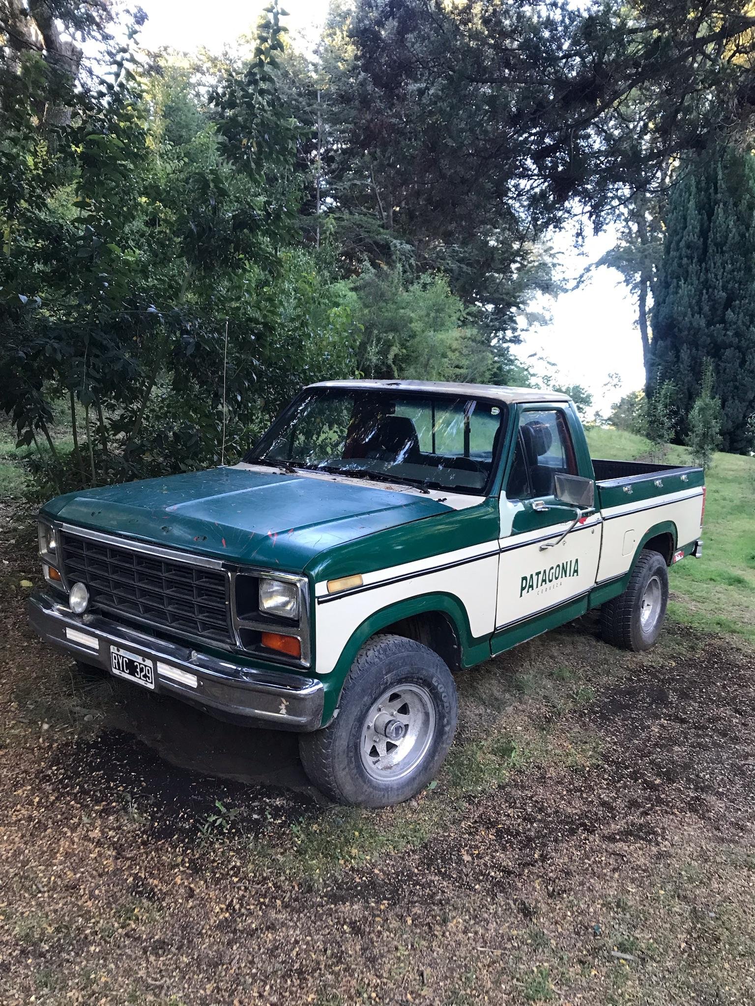 Entrada da Cervejaria Patagonia em Bariloche, com um carro antigo decorativo verde estacionado na frente e vista para as montanhas.